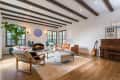 Cozy living room with wooden beams, fireplace, leather sofa, armchairs, piano, and a guitar.