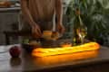Person setting table with glowing baguette lamp, wine, salad, and rolls.