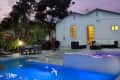 Modern backyard with illuminated pool, patio dining set, and white sofa near a white house at dusk.