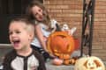 Two children sitting on steps with carved pumpkins and small painted pumpkins for Halloween.