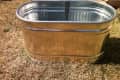 Galvanized metal tub on dry grass in a backyard setting.