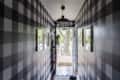 Hallway with black and white checkered walls, framed pictures, and a view of a tree through the open door.