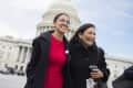 Two women smiling in front of the U.S. Capitol building, one in a red dress and the other in a black coat holding a cup.