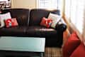 Black leather sofa with colorful pillows, teal coffee table, and wall art in a bright living room.