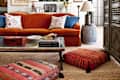 Eclectic living room with orange sofa, patterned cushions, glass coffee table, and decorative lamps.