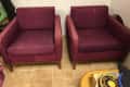 Two maroon armchairs with wooden legs on a tiled floor, next to a stack of items.