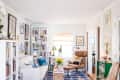 Cozy living room with white sofa, bookshelves, brown leather chair, colorful cushions, and a geometric blue rug.