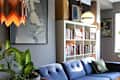 Mid-century modern living room with blue sofa, abstract art, bookshelves, and a large potted plant.