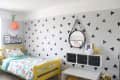 Kids' room with yellow bed, triangle-patterned wall, round mirror, and colorful bedding. Decor includes animal toys and art.