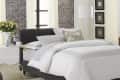 Cozy bedroom with a black bed, white bedding, gray rug, and a side table with flowers and a coffee set.