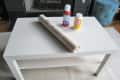 White coffee table with a roll of contact paper, spray adhesive, and Mod Podge bottle on top.