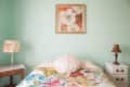 Bedroom with floral bedspread, mint green walls, floral lampshade, and framed flower artwork above the bed.