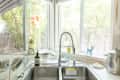Kitchen sink with a modern faucet, soap dispenser, and window view of bamboo plants.