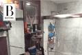 Cluttered bathroom with marble countertop, shower with glass doors, and various toiletries on shelves and sink.