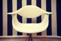 White modern chair with curved arms in front of a navy and white striped wall.