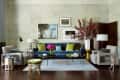 Elegant living room with blue velvet sofa, green cushions, floral decor, and framed art on light walls.