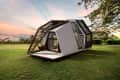 Modern geometric tiny house with large windows on a grassy field at sunset.