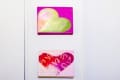 Four colorful heart-themed artworks on a white wall, each with unique patterns and vibrant colors.