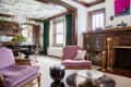 Living room with purple armchairs, a round glass coffee table, brick fireplace, and green curtains.