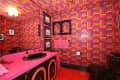 Vibrant bathroom with pink and orange geometric wallpaper, pink countertop, black sink, and framed art on walls.
