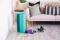 Yoga mat, water bottle, and sneakers on floor near a pink sofa with decorative pillows and a side table with books.
