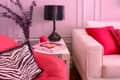 Living room with pink walls, red chair, zebra pillow, white sofa, black lamp, and colorful art print.