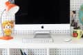 A white work desk displaying an iMac computer in the middle, a small orange lamp, and a pen holder on opposite sides