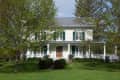 Two-story white house with green shutters, surrounded by trees and a well-kept lawn.