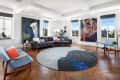 Spacious living room with modern art, gray sectional sofa, blue chairs, and a round abstract rug on wooden flooring.