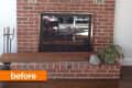 Red brick fireplace with glass doors, flanked by two vents, a plant, and a candle holder on a wooden floor.