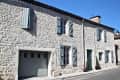 Stone house with blue shutters, garage door, and potted plants on a sunny street.