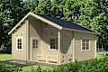 Small wooden cabin with a front porch, surrounded by lush green trees and grass.
