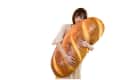 Woman hugging a giant baguette-shaped pillow, wearing a light-colored dress.