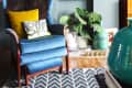 Blue armchair with yellow and patterned cushions, large wall clock, bookshelf, and potted plant on wooden floor.