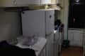 Narrow kitchen with white cabinets, fridge, stove, and a window.