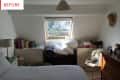 Attic bedroom with sloped ceiling, skylight, cluttered shelves, and a bed with white bedding.