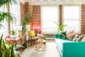 Bright living room with teal sofa, colorful pillows, plants, brick walls, and a neon "Fantasy" sign.