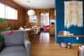Mid-century modern living room with gray armchair, wooden dining table, blue accent wall, and woven wall hanging.