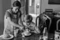 Woman helping a boy with breakfast at a wooden table, featuring pastries, milk, and a vintage radio in the background.