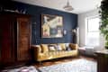 Living room with a mustard yellow sofa, eclectic artwork, wooden armoire, and a large window with plants.