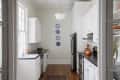 Narrow kitchen with white cabinets, black countertops, orange kettle, and blue decorative plates on the wall.