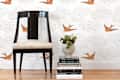 Black chair with cream cushion next to a stack of books and a vase of succulents, against bird-patterned wallpaper.