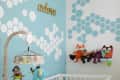 Baby nursery with blue hexagon wall design, white crib, hanging toys, and plush animals on the wall.