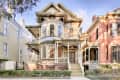 Victorian-style house with ornate trim, large bay windows, and a covered porch, flanked by brick and wood siding.