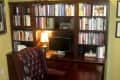 Home office with dark wood desk, leather chair, bookshelves filled with books, and a small lamp on the desk.