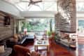 Spacious living room with stone fireplace, leather sofa, wooden coffee table, and large windows overlooking a garden.