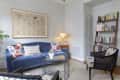 Blue velvet sofa with patterned pillows, abstract wall art, bookshelf, and modern chairs in a cozy living room.