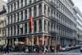 Historic cast-iron building with ornate facade, fire escape, and busy street corner with pedestrians and cars.