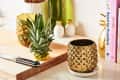Pineapple on a cutting board with a knife, next to a gold pineapple-shaped mug and cookbooks.