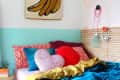 Colorful bedroom with heart-shaped pillows, banana wall art, and headphones hanging on a slatted headboard.